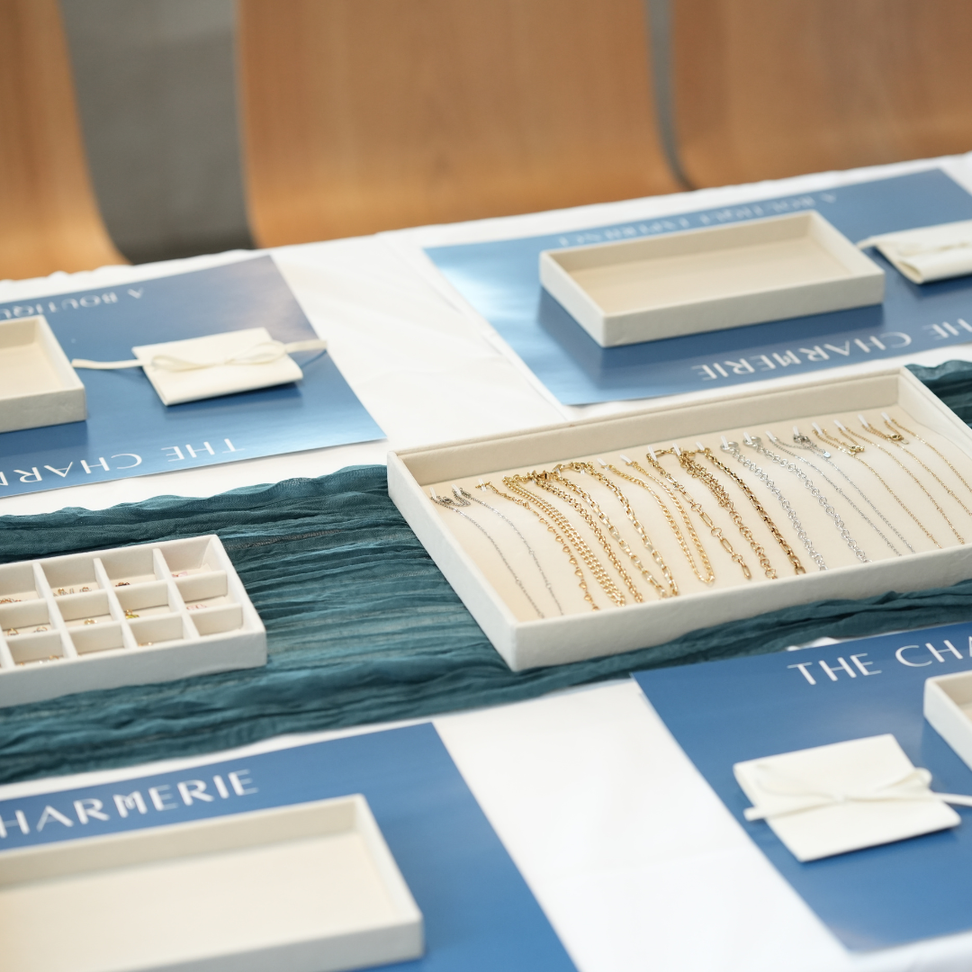 Jewelry display with necklaces on a branded tablecloth, featuring the brand 'The Charmerie'.